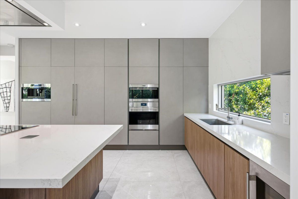 Panel-ready refrigeration and Wolf wall ovens beside a garden-view window